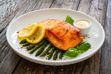 Fried salmon steak with cooked green asparagus and mayonnaise served on wooden table
