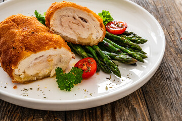 Cutlet de Volaille, wrapped chicken cutlet served with cooked green asparagus on wooden table
