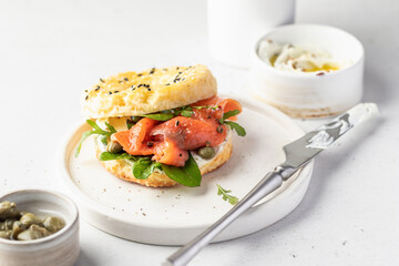Homemade bagel sandwich with smoked salmon, cream cheese, capers and spinach for healthy breakfast on white kitchen background, text space