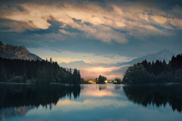 Night scenery with illuminated clouds reflected in a lake. A tranquil Alpine landscape in blue and yellow tones