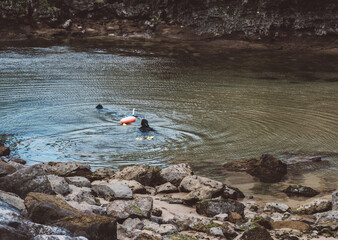 Two Scuba Divers Exploring Tranquil Waters Near Rocky Shoreline During Daylight