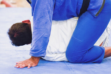 Two unidentifiable men practicing Brazilian Jiu-Jitsu on a blue mat