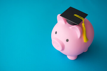 Pink piggy bank and mortarboard on blue background with copy space. Money savings and financial...