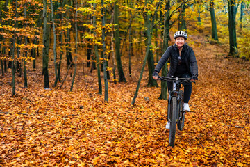 Mid-adult woman riding bicycle in city forest in autumnal scenery
