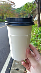 A person is holding a white coffee cup with a lid on it