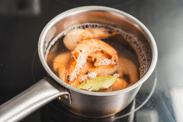 Large shrimp are boiled in water with bay leaves. A saucepan on an induction hob with boiled king...