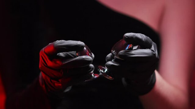 Two metal anal plug in female hands in black latex gloves and a black dress on a red background. Sex shop, Adult store. BDSM - outfit for adult sex games
