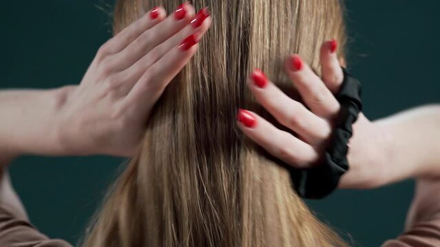 Rear view of woman tying hair ponytail with black elastic band. Hair care concept
