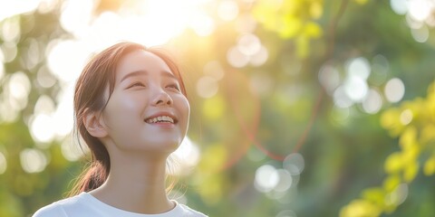 Fototapeta premium Asian Woman Smiling Under Bright Sunlight, Eyes Closed, Feeling Peace and Positivity