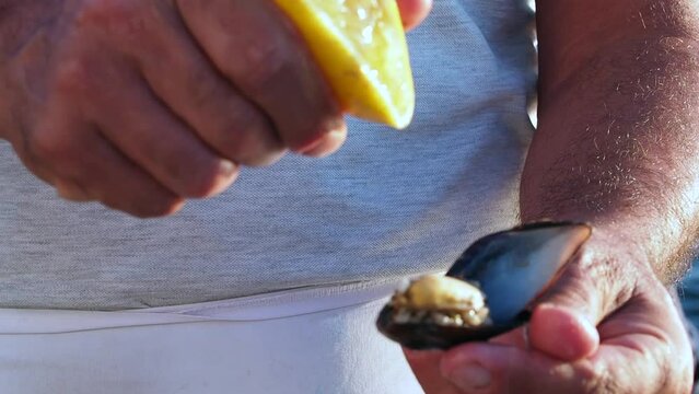 The man opens the mussels and squeezes lemon.