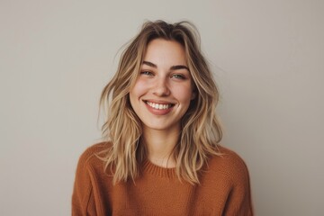 Obraz premium Happy young woman with blonde hair, smiling cheerfully at camera in casual outfit. Stunning female model posing with joy against white studio background