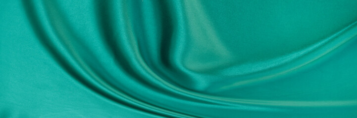 Black green satin dark fabric texture luxurious shiny that is abstract silk cloth background with patterns soft waves blur beautiful.