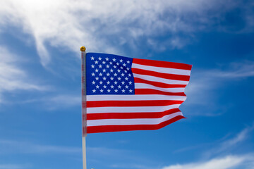 Obraz premium American flag fluttering in the wind against blue sky and white clouds