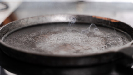 A mottled cast iron frying pan is smoking on the stove. A frying pan ready to cook. selected focus.