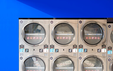 Rows of vending washing machines and clothes dryers on blue smartboard wall background in modern...