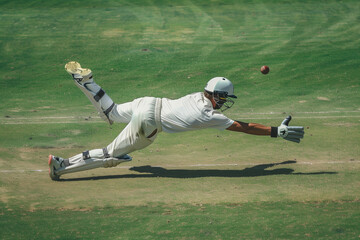 Obraz premium A man in a white shirt and white pants is crouching on the ground, holding a cricket glove. 
