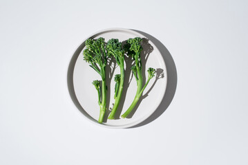 Brócoli broccolini bebé crudo dentro de un plato sobre fondo blanco. Vista superior