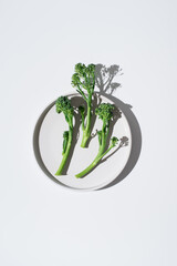 Brócoli broccolini bebé crudo dentro de un plato sobre fondo blanco. Vista superior