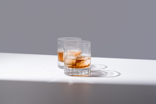 Dos vasos de whisky con hielo sobre un fondo gris	
