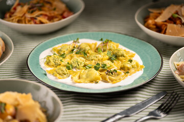 Italian ravioli with spinach and cheese on blue plate serving at table with other dishes. Italian cuisine concept.