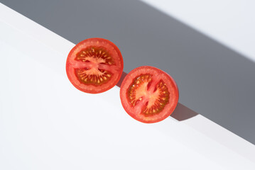 Un tomate maduro cortado por la mitad sobre un soporte blanco y fondo gris	