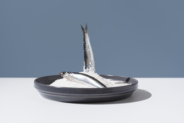 Dos anchoas frescas dentro de un plato lleno de sal sobre fondo azul	