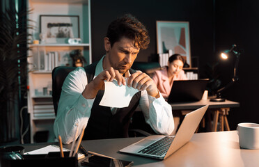 Sitting man with serious face tearing failure paperwork of business project at night lighting time...