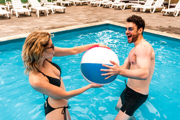 Happy couple of vacationists in sunglasses playing a water game in an outdoor pool. Summer fun and leisure activity concept