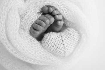 The tiny foot of a newborn baby. Soft feet of a new born in a wool blanket. Close up of toes, heels and feet of a newborn. Knitted heart in the legs of a baby. Black and white Macro photography. 