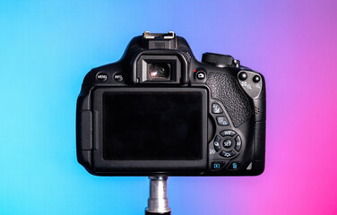 Black digital camera photograph from behind, view of buttons, camera screen, viewfinder and grip. Coloured background.