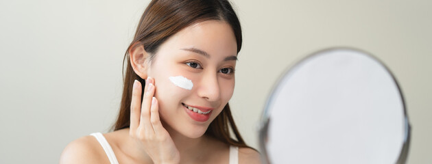 wellness care concept,  young woman looking at the mirror and applying facial skin care cream on...