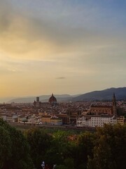 Fototapeta premium Sunsets over Florence! The terracotta dome of the Duomo crowns the city bathed in golden light. Visitors admire the view from a terrace, their silhouettes contrasting the vibrant sky.