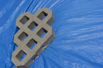 chunk of turf pavers (grid-like pattern with voids) made of cement and placed on blue tarp 