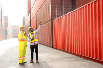 Two diverse container workers working at dock site,foreman control loading containers box from cargo freight ship holding walkie talkie,african male using digital tablet inspect cargo container boxes