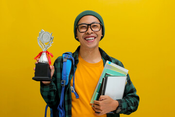 Asian student, dressed in a beanie hat and casual shirt, holds books and a trophy, celebrating the success of winning and achievements, depicted against a yellow background