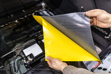 Auto service worker installing soundproofing foam material on car door trim from inside, tuning car...
