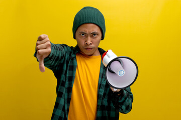 Displeased Asian man in a beanie hat holds a megaphone with an angry face, showing a thumbs-down to...