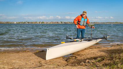 Senior male rower with his rowing shell on a beach of Boyd Lake in northern Colorado, serly spring...