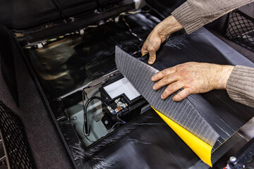 Auto service worker installing soundproofing foam material on car door trim from inside, tuning car...
