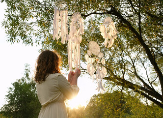 summer. girl in light dress and dream catchers hanging on tree outdoor, sunny natural background....