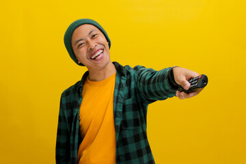 Excited Asian man, dressed in a beanie hat and casual shirt, watches a TV show or movie, pressing a...