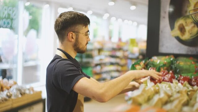 A guy working at a store is sorting products on the shelves. A man packs pasta on store shelves