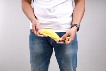 Asian man measuring a banana using tape measure on his crotch. Size matters concept and penis size...