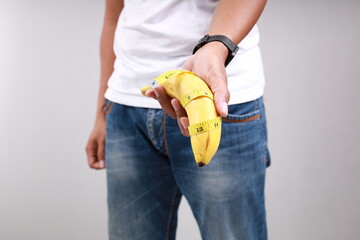 Asian man holding a banana with tape measure. Size matters concept and penis size measurement.