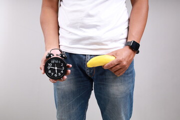 Asian man holding a yellow banana and alarm clock. Erection time and erection endurance time concept