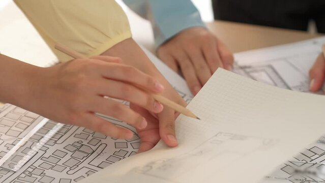 Smart architect and safety engineer discussion about building blueprint on table with architectural document, measurement tools and wooden block scatter around at modern office. Closeup. Delineation.