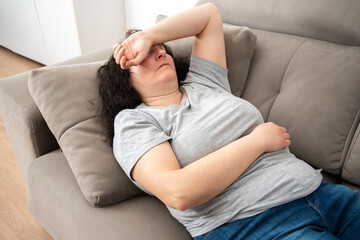 Woman lying on back on comfortable couch at home, covering eyes with hand, sleeping at daytime,...