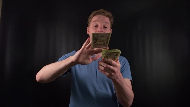 a dashing young man enthusiastically counts a stack of dollar bills. The thrill of a life-changing stroke of luck on the simple black backdrop. The epitome of celebratory joy after hitting the jackpot