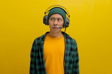 Asian man in a casual clothes, wearing headphones, looks up in deep thought, seemingly troubled by...