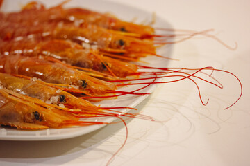 Fresh orange boiled king shrimps on a white plate on a table. Whole cooked delicious seafood served in restaurant. Large prawns with long mustache.